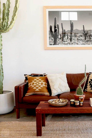 P.F. Candle Co No.22 Mojave Candle 7.2oz in a home setting with brown sofa and table with cactus plants and cactus photo frame hung up