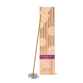 Palo santo incense sticks in a beige and purple box with foiled Japanese Zen stone garden patterns, with one stick propped on an aluminum incense holder in front of the box.