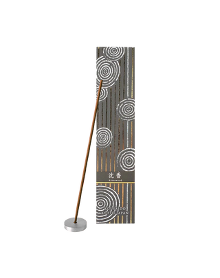 Agarwood incense sticks in a black and white box with foiled Japanese Zen stone garden patterns, with one stick propped on an aluminum incense holder in front of the box.