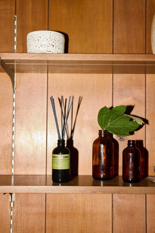 P.F. Candle Co Geranium Moss reed diffuser with reed sticks in a 103ml glass bottle, placed on a Nordic minimalist shelf beside two apothecary jars with green plants