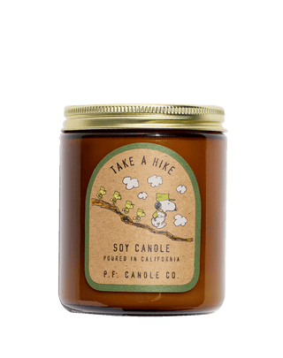A soy candle in a amber jar with a brown label featuring illustrations of Snoopy and Woodstock from Peanuts. The label has a 'Take A Hike' theme with a green and beige color scheme.