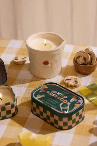 Paddywax Wild Mushroom Bistro Collection ceramic candle styled on checkered table with sliced mushrooms and matching tin candle, warm cozy scene evoking woodland aroma and rustic kitchen gift inspiration.